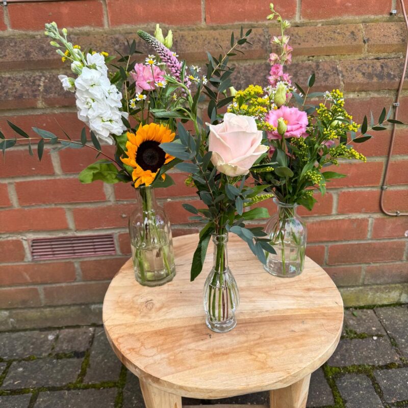 A cluster glass bud bottles filled with seasonal flowers. Select your colour colour palette. Order online for next day delivery.