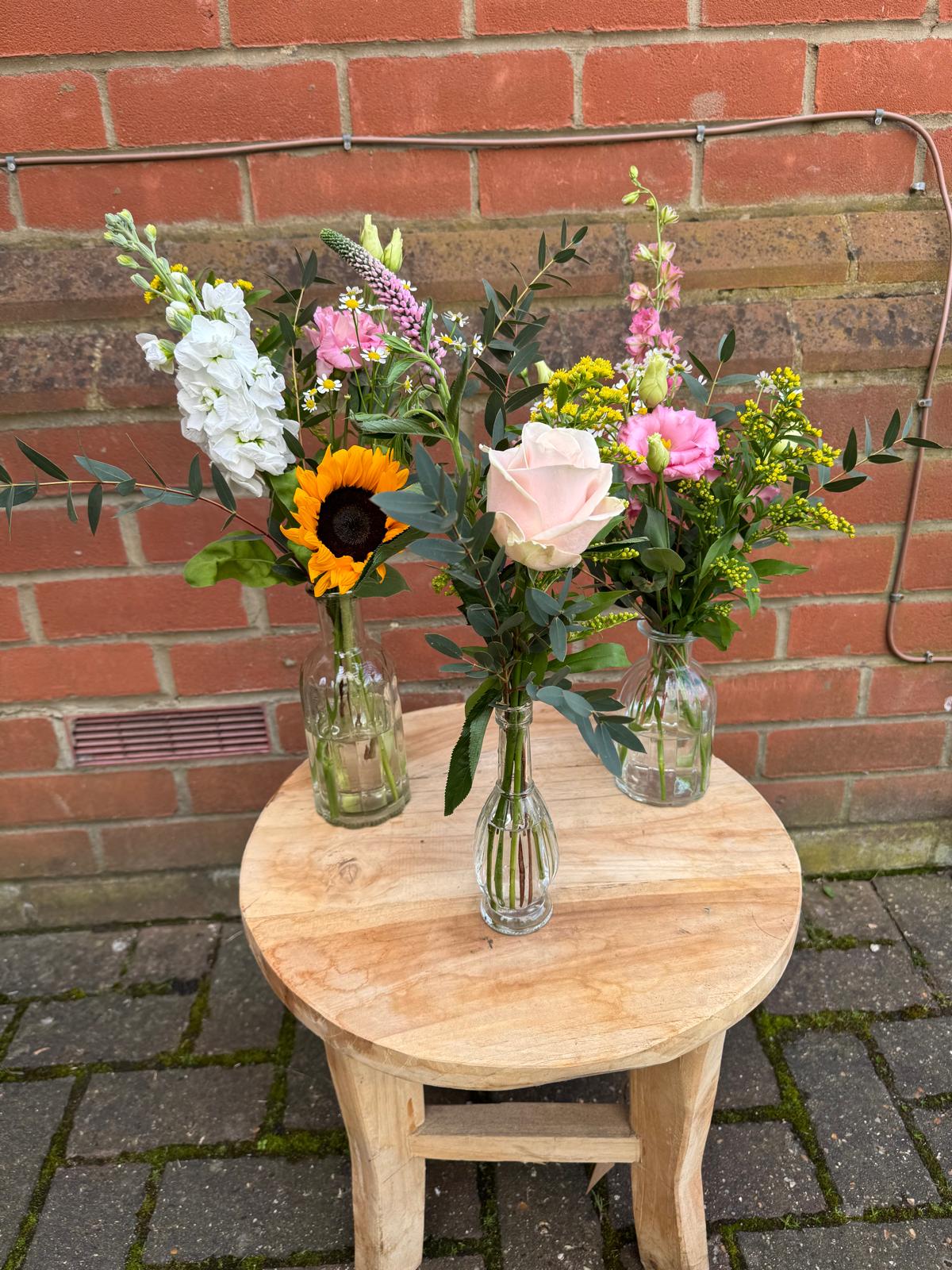 A cluster glass bud bottles filled with seasonal flowers. Select your colour colour palette. Order online for next day delivery.